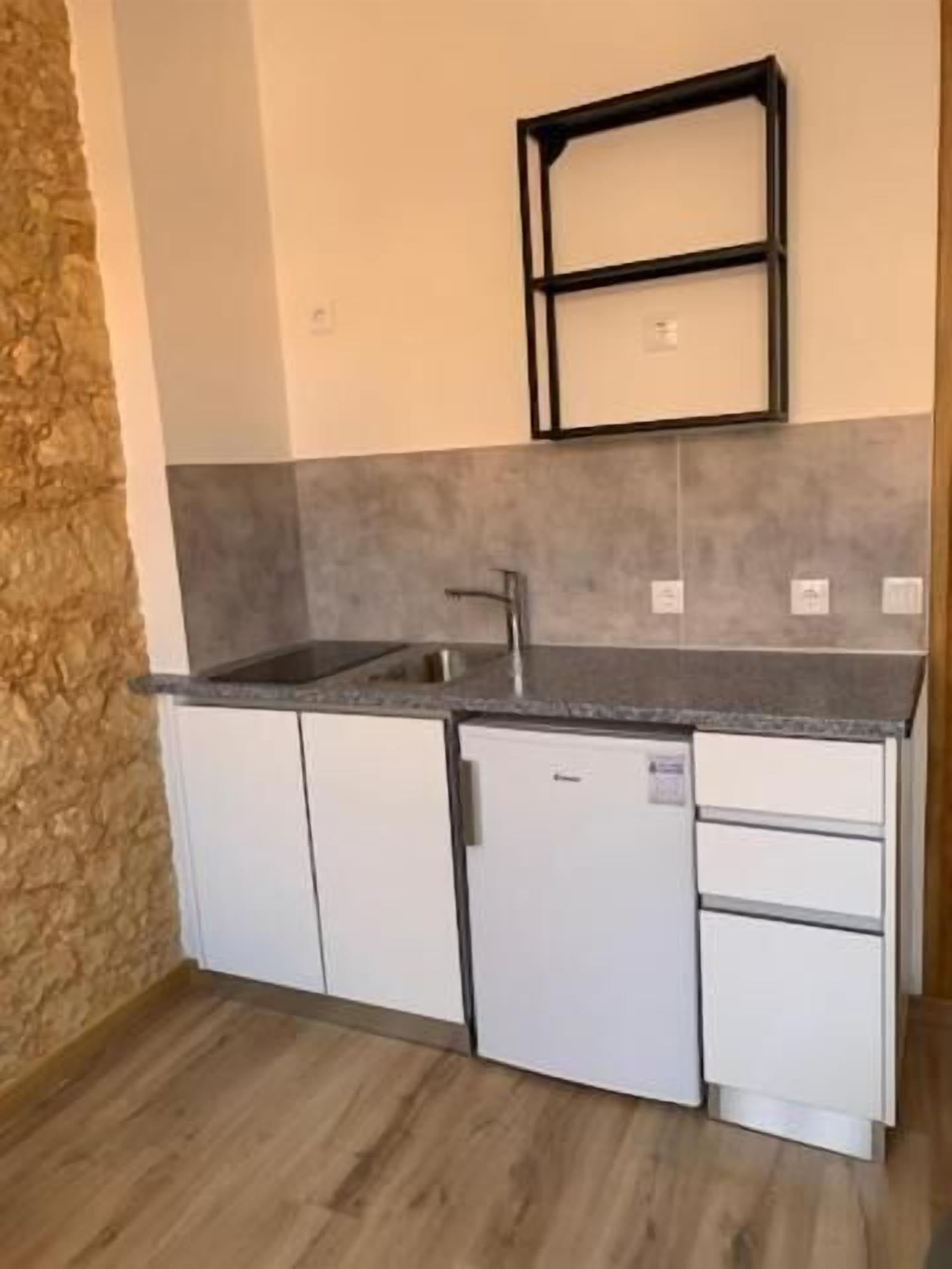 A compact kitchen with white cabinets, a granite countertop, and a black metal shelf above the sink.