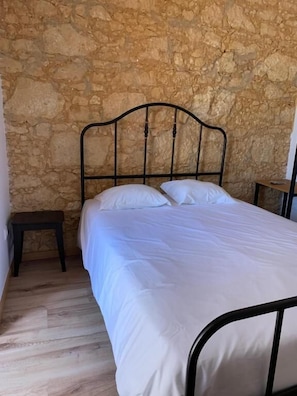 A bedroom with a stone wall, a metal bed frame, white bedding, and a small wooden nightstand. - Quimpecável (Figueira da Foz)