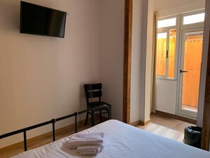 Ein Schlafzimmer mit Bett, Sessel, Wand-Fernseher und Fenster mit Blick auf eine Holzlattenveranda.