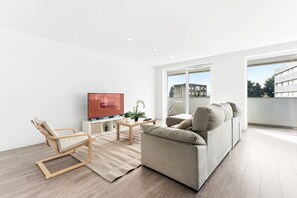 Un salon moderne avec un canapé, une table basse, un téléviseur et un fauteuil.