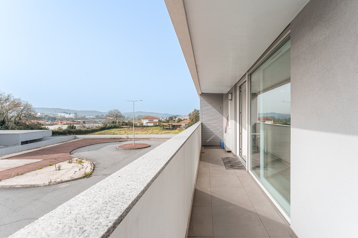 A modern building with a balcony overlooking a parking area and distant landscape.