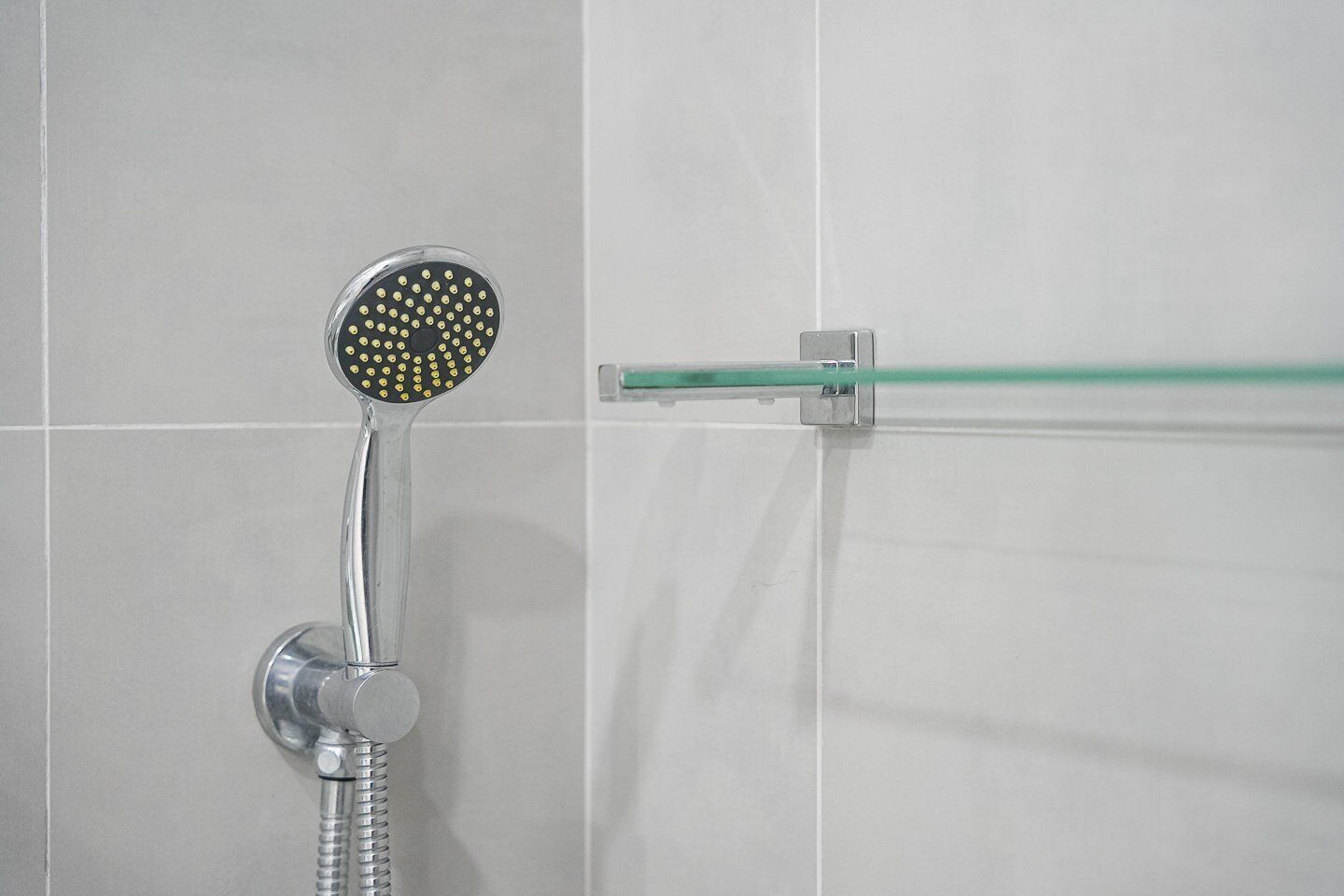 Une douche dotée d’un pommeau rond et d’une barre de douche en verre.
