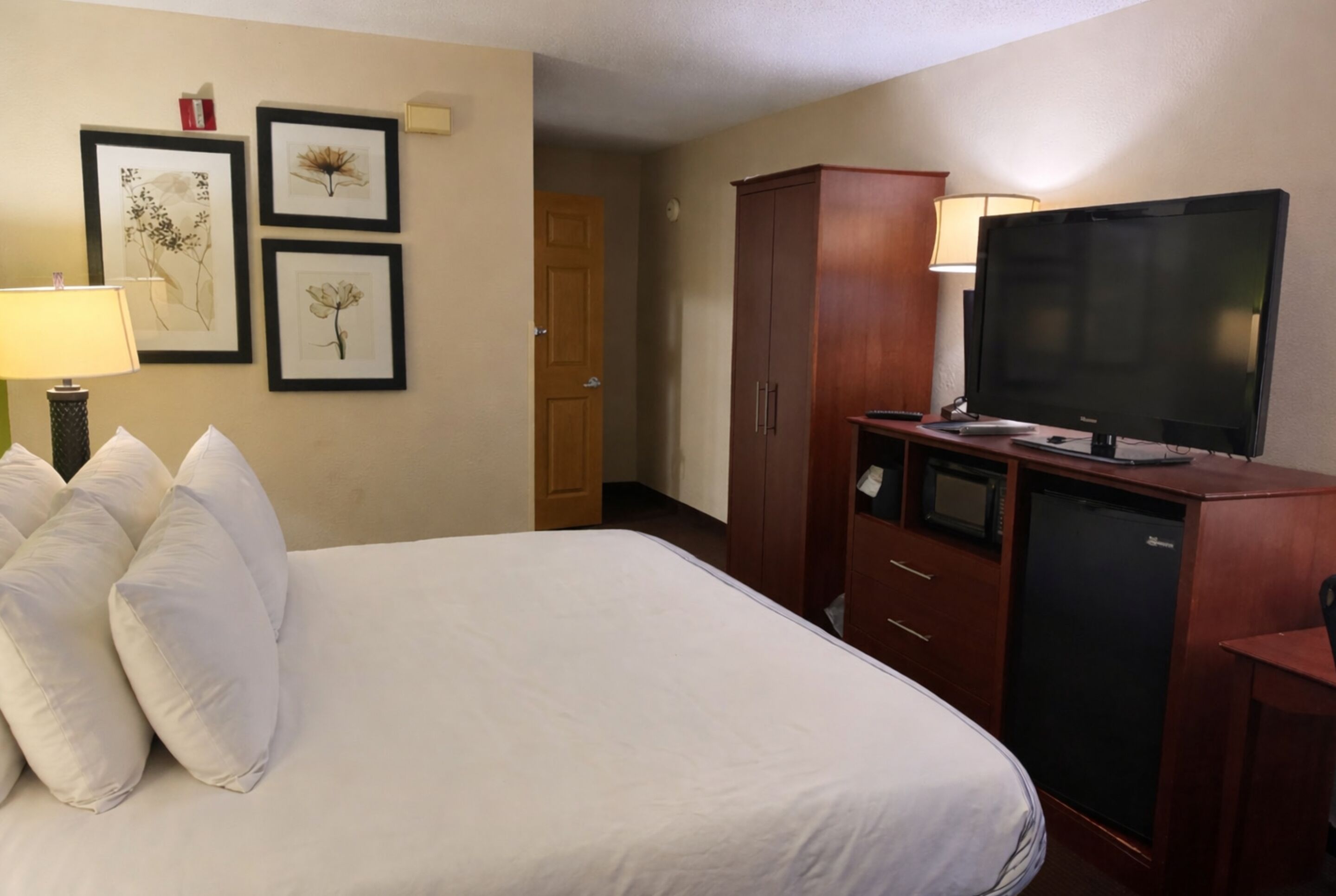 A hotel room with a bed, a television, a wardrobe, and framed pictures on the wall.