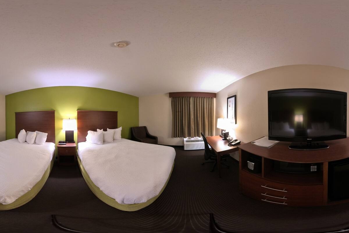 A hotel room with two beds, a desk, a television, and a chair.