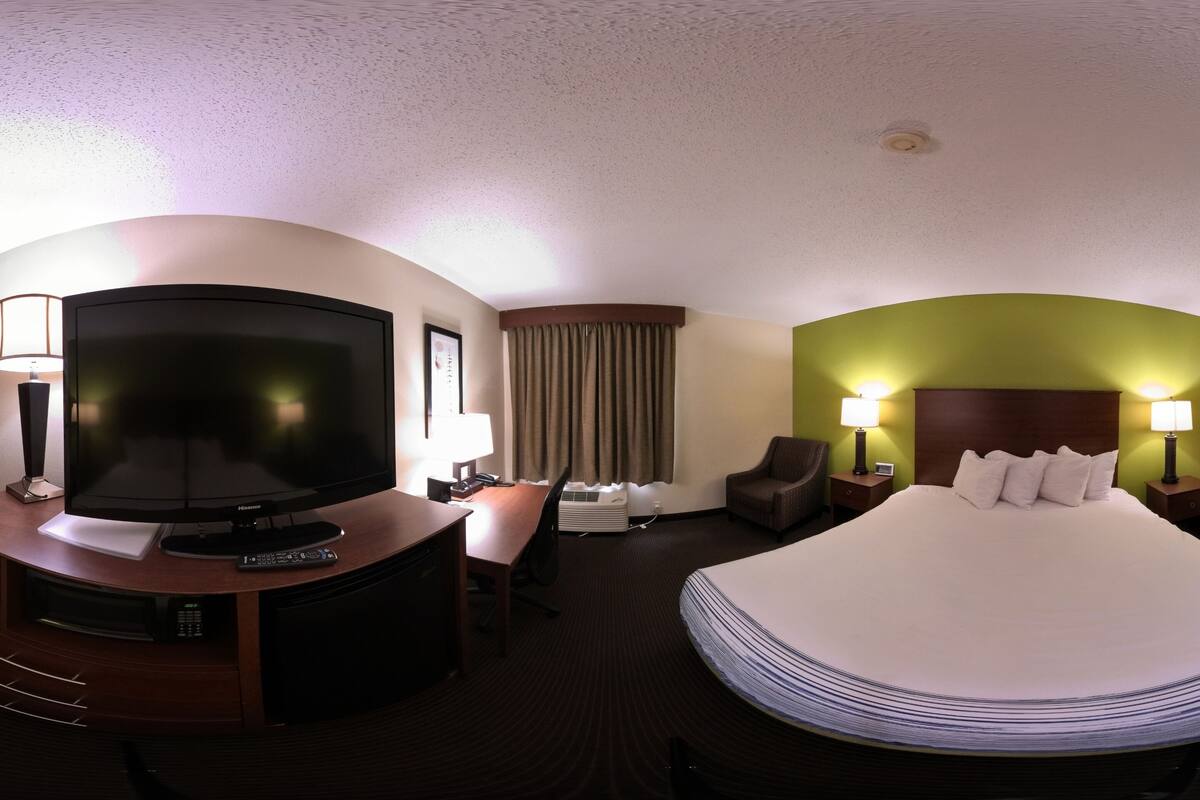 A hotel room with a bed, TV, desk, chair, and lamps.