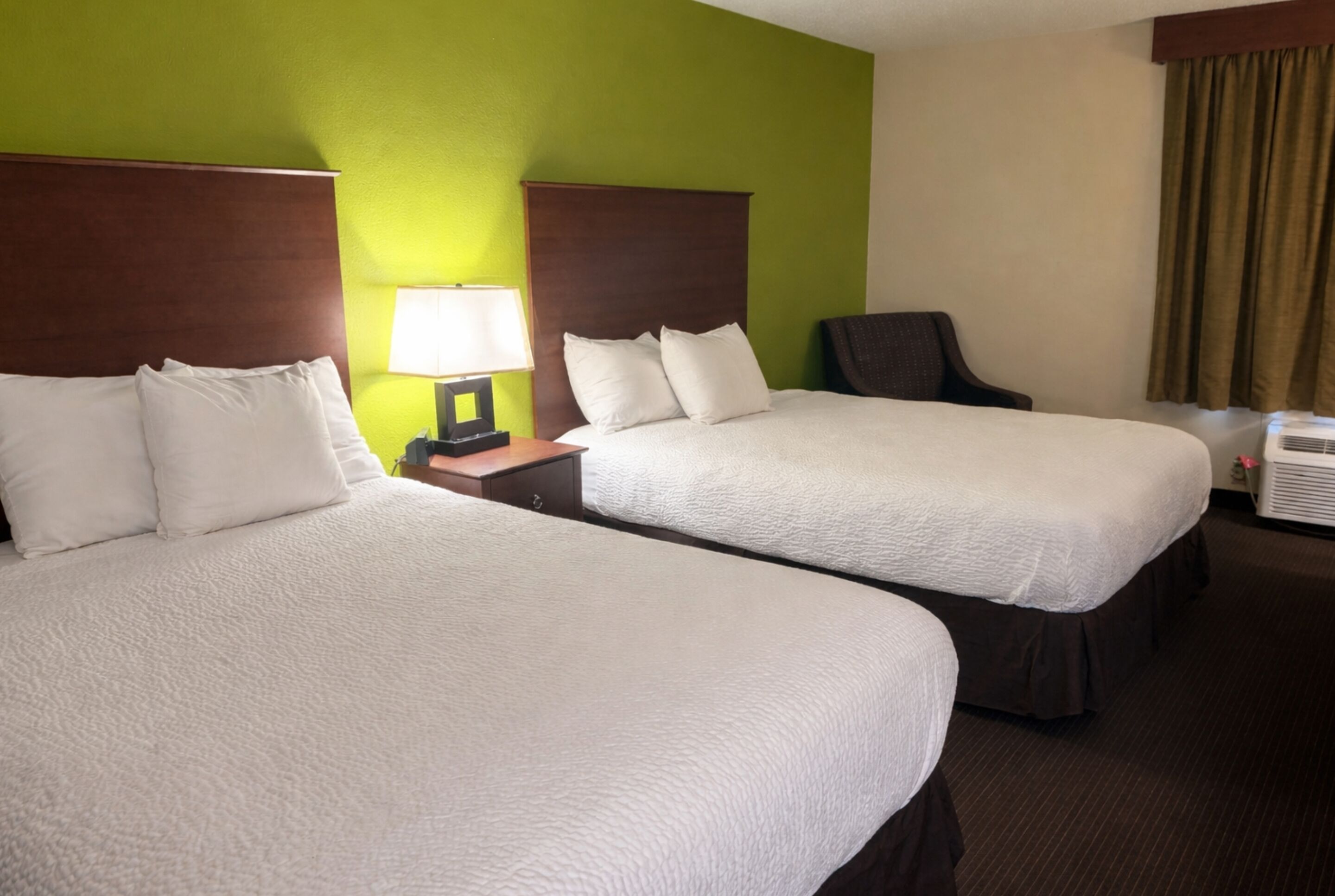 Two beds with white bedding, a nightstand with a lamp, a chair, and an air conditioning unit.