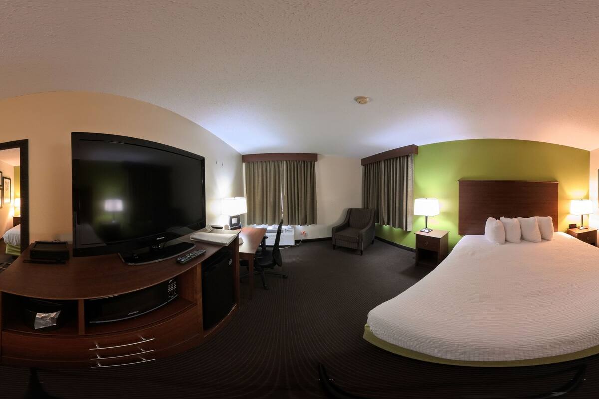 A hotel room with a bed, television, desk, chair, and lamps.