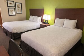 Two twin beds with white bedding, a nightstand with a lamp, and framed artwork on the wall. - Coratel Plus Suites by Jasper Black River Falls (Black River Falls)