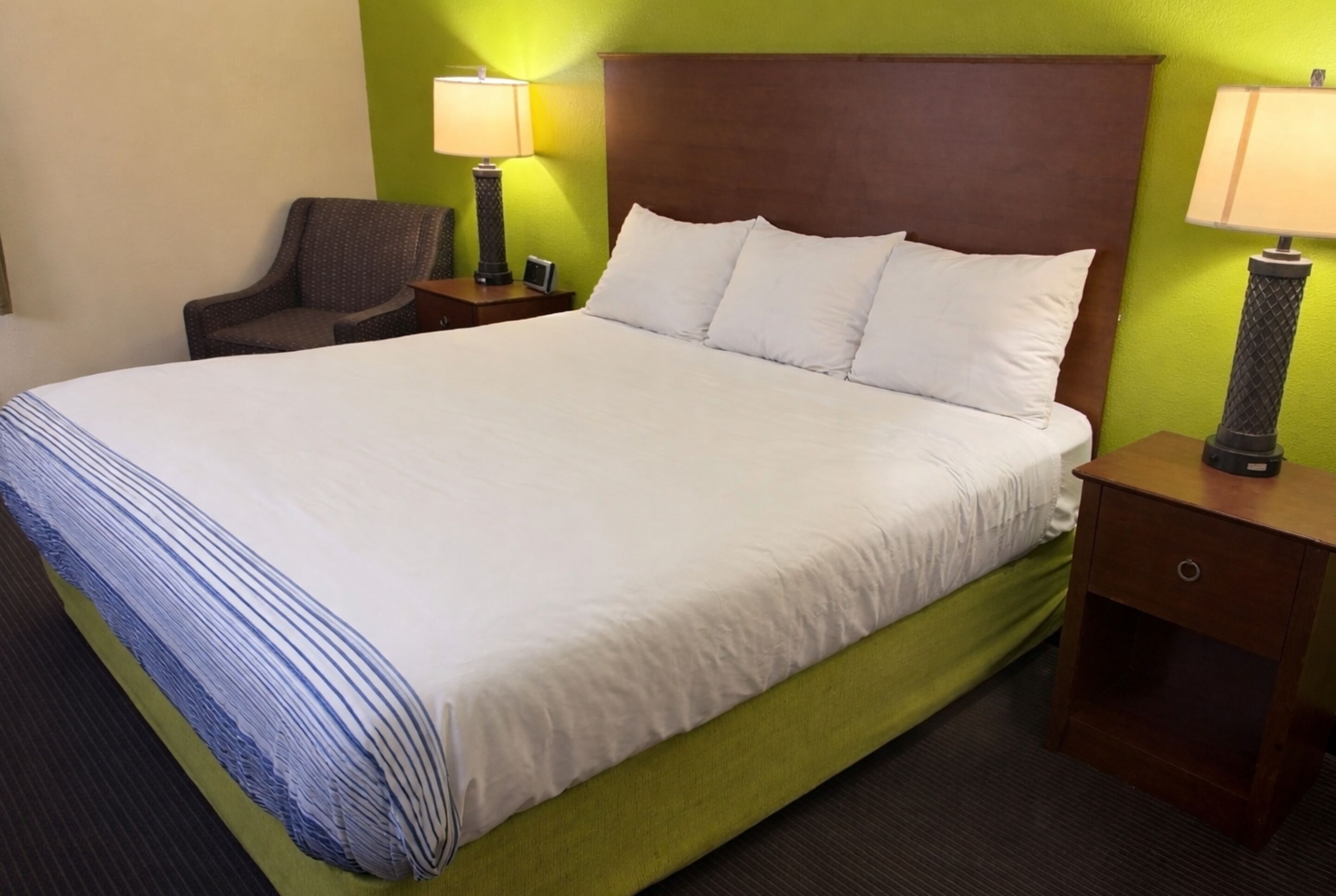 Una habitación de hotel con una cama grande, dos mesitas de noche, una silla y paredes verdes.