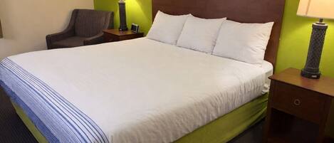 Una habitación de hotel con una cama grande, dos mesitas de noche, una silla y paredes verdes.