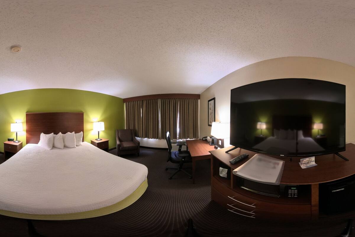A hotel room with a large bed, a desk with a TV, a chair, and a desk lamp.