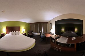 A hotel room with a large bed, a desk with a TV, a chair, and a desk lamp. - Coratel Plus Suites by Jasper Black River Falls (Black River Falls)