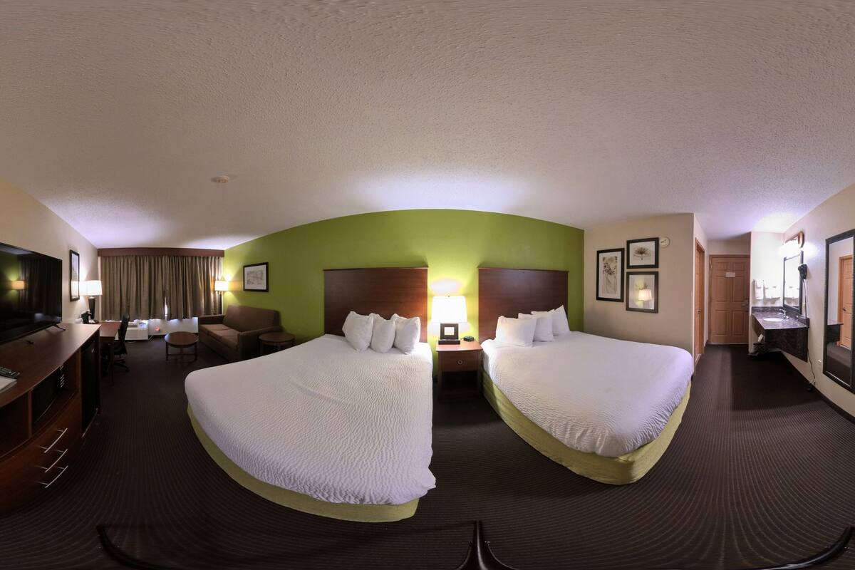 A hotel room with two beds, a desk, a chair, a TV, and a bathroom.