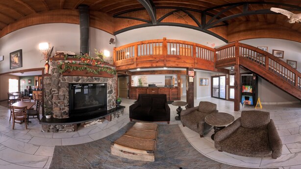 A spacious living area with a fireplace, wooden staircase, and a high ceiling. - Coratel Plus Suites by Jasper Black River Falls (Black River Falls)