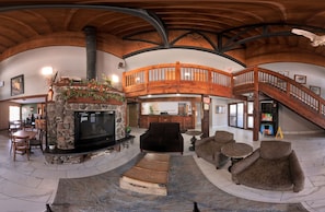 A spacious living area with a fireplace, wooden staircase, and a high ceiling. - Coratel Plus Suites by Jasper Black River Falls (Black River Falls)