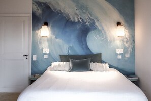 Ein Schlafzimmer mit einem großen Bett, zwei Wandleuchten und einem Wandgemälde von einer Welle.