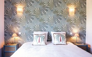 Ein Bett mit zwei Kissen, eine Wand mit Blattmuster und zwei Wandlampen.