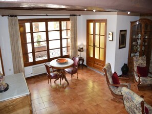 Une pièce comprenant une table à manger, des chaises, un radiateur, une fenêtre avec des rideaux, une porte et un meuble avec des portes en verre.