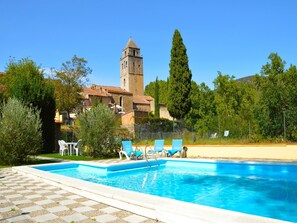 Une piscine avec des chaises longues, une haute tour et un bâtiment doté d’un toit recouvert de tuiles rouges.