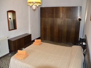 Une chambre d’hôtel avec un grand lit, une tête de lit en bois, une commode, un miroir et un radiateur.