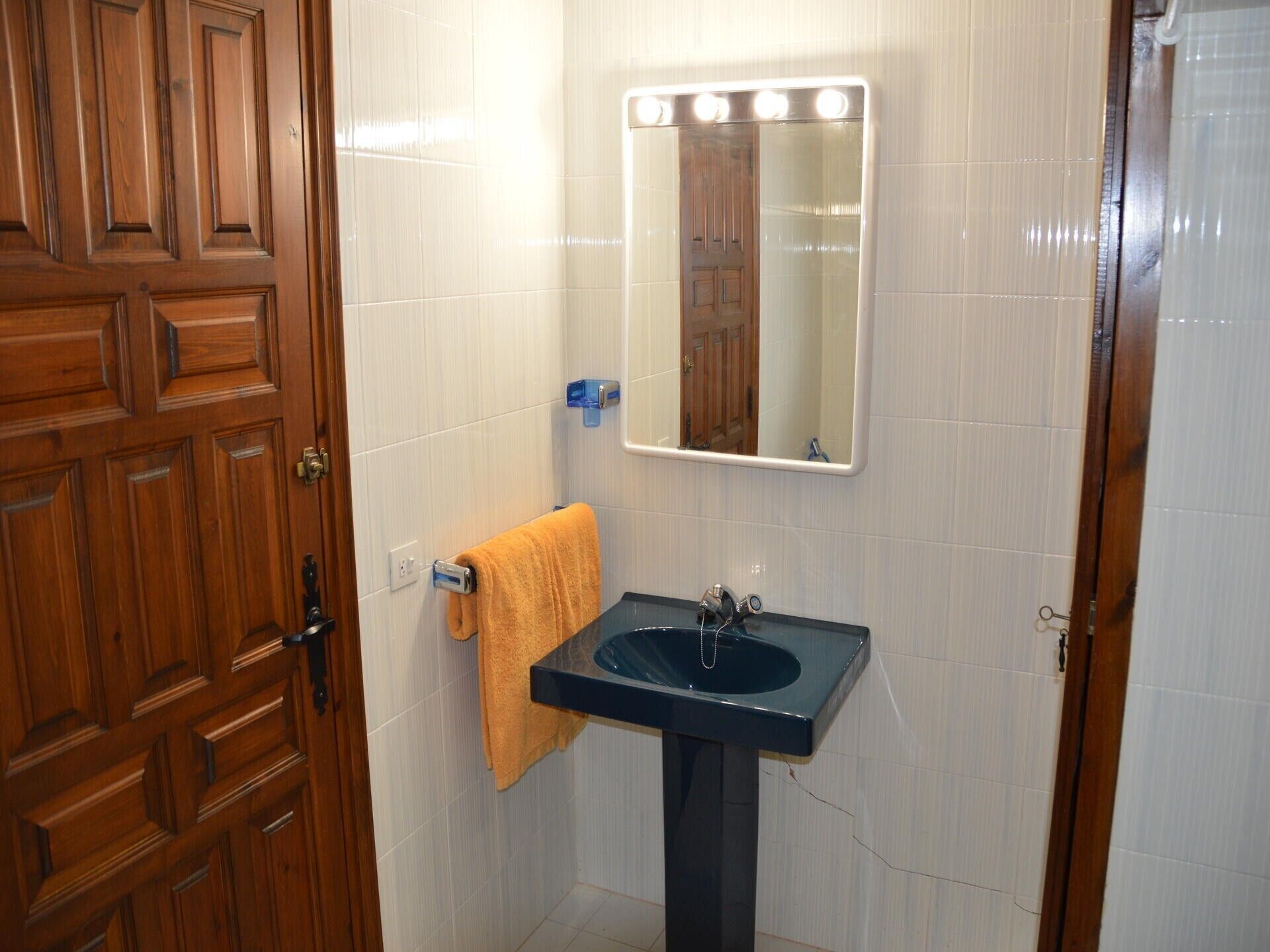 A bathroom with a wooden door, a sink with a mirror above it, and a towel hanging on the wall.