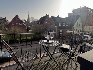 A balcony with a table and chairs, overlooking a residential street with houses and parked cars. - Cozy apartment in Emden, 5 minutes to the city center (Emden)