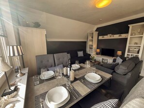 A dining area with a table set for four, including plates, glasses, and cutlery. There is a sofa and a television in the background. - Cozy apartment in Emden, 5 minutes to the city center (Emden)