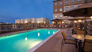 A swimming pool with lounge chairs and umbrellas, surrounded by a fence and a building with multiple windows. - Odessa 1BR Suite w/ Kitchen | Breakfast Included (Odessa)