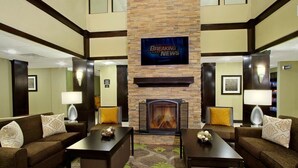 A hotel lobby with a fireplace, two sofas, a coffee table, and a television displaying 'Breaking News'. - Odessa 1BR Suite w/ Kitchen | Breakfast Included (Odessa)