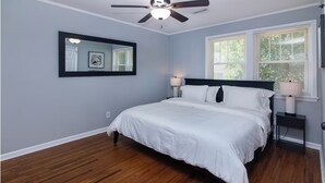 A bedroom with a bed, a ceiling fan, a nightstand with a lamp, and a window with blinds. - Charming 3BR Retreat in Plaza Close to Uptown (Charlotte)