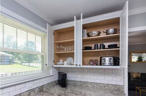 A kitchen with white cabinets, a coffee maker, and a window with blinds. - Charming 3BR Retreat in Plaza Close to Uptown (Charlotte)
