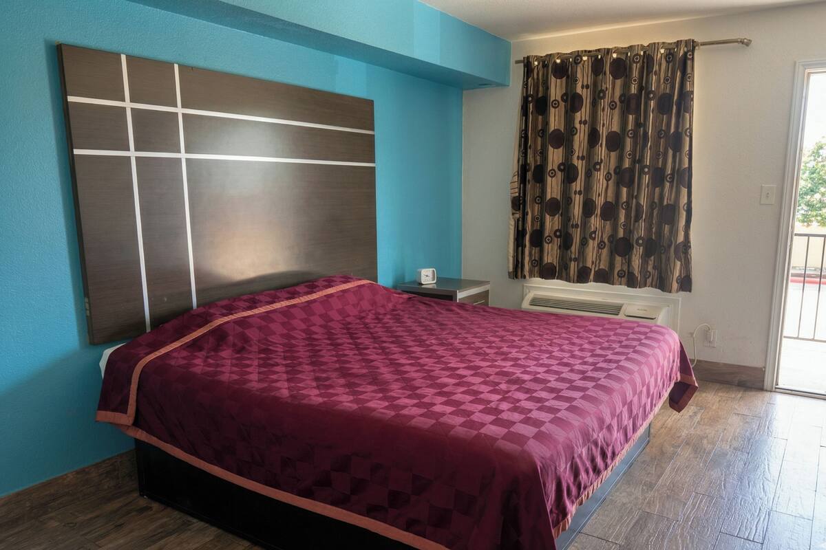 Un dormitorio con cama, mesita de noche, calefactor y ventana con cortinas.