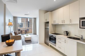 Een moderne keuken met een inbouwoven, een roestvrijstalen koelkast en een magnetron. Er is een zithoek met een tafel en stoelen, en een groot raam met uitzicht op de stad.