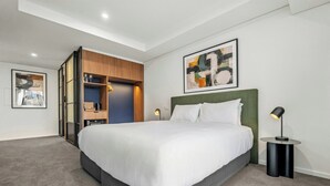 A modern hotel room with a large bed, a built-in wardrobe, a bedside table, and a floor lamp. - Oaks Melbourne on Lonsdale Suites (Melbourne)