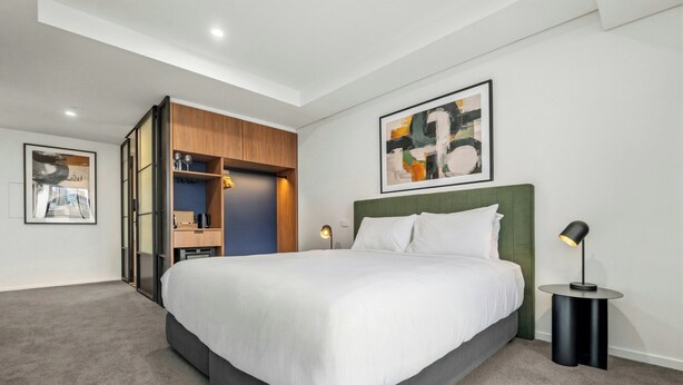 Een moderne hotelkamer met een groot bed, een inbouwkast, een nachtkastje en een vloerlamp.