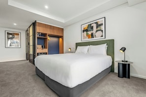 A modern hotel room with a large bed, a built-in wardrobe, a bedside table, and a floor lamp. - Oaks Melbourne on Lonsdale Suites (Melbourne)