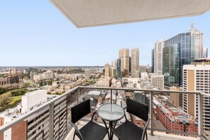 Un balcón con una mesa y sillas, con vista a un paisaje urbano con varios edificios.
