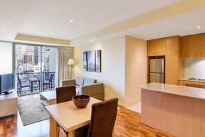 A modern apartment with a dining area, kitchen, and a balcony with a city view. - Oaks Melbourne on Lonsdale Suites (Melbourne)