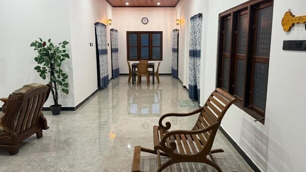 A hallway with a wooden bench, a potted plant, a dining table with chairs, and a window with curtains. - Palm Breeze kokuvil Jaffna (Kokuvil East)
