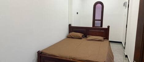 Un dormitorio con una cama de madera, un ventanal pequeño y una puerta.