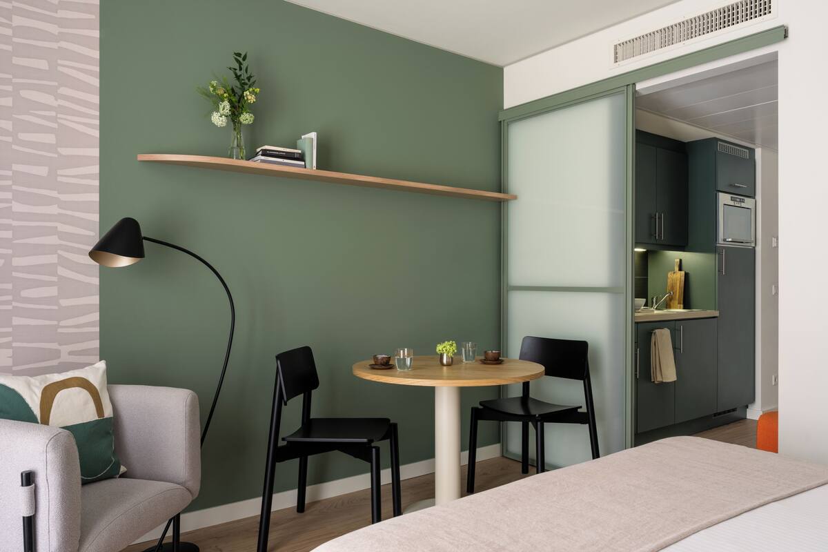 Une pièce moderne comprenant une table ronde, deux chaises, un canapé, un lampadaire, une bibliothèque et un coin cuisine.