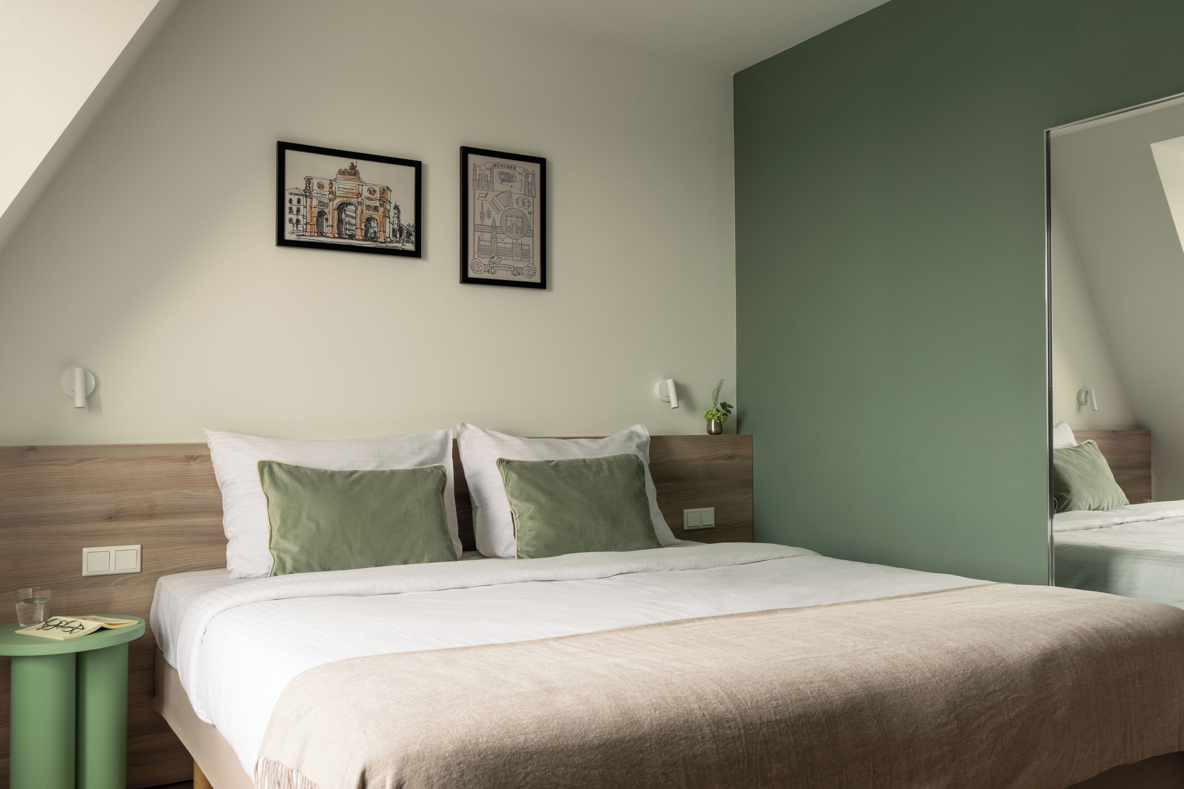 A hotel room with a bed, a round side table, a mirror, and two framed pictures on the wall.