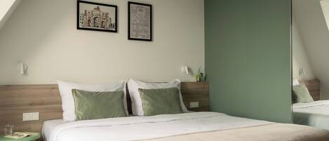 A hotel room with a bed, a round side table, a mirror, and two framed pictures on the wall.