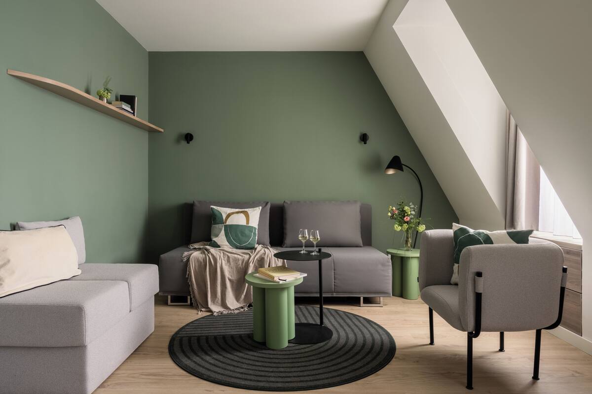 Un salon moderne avec un canapé gris, un fauteuil vert, une table basse ronde et un lampadaire noir.