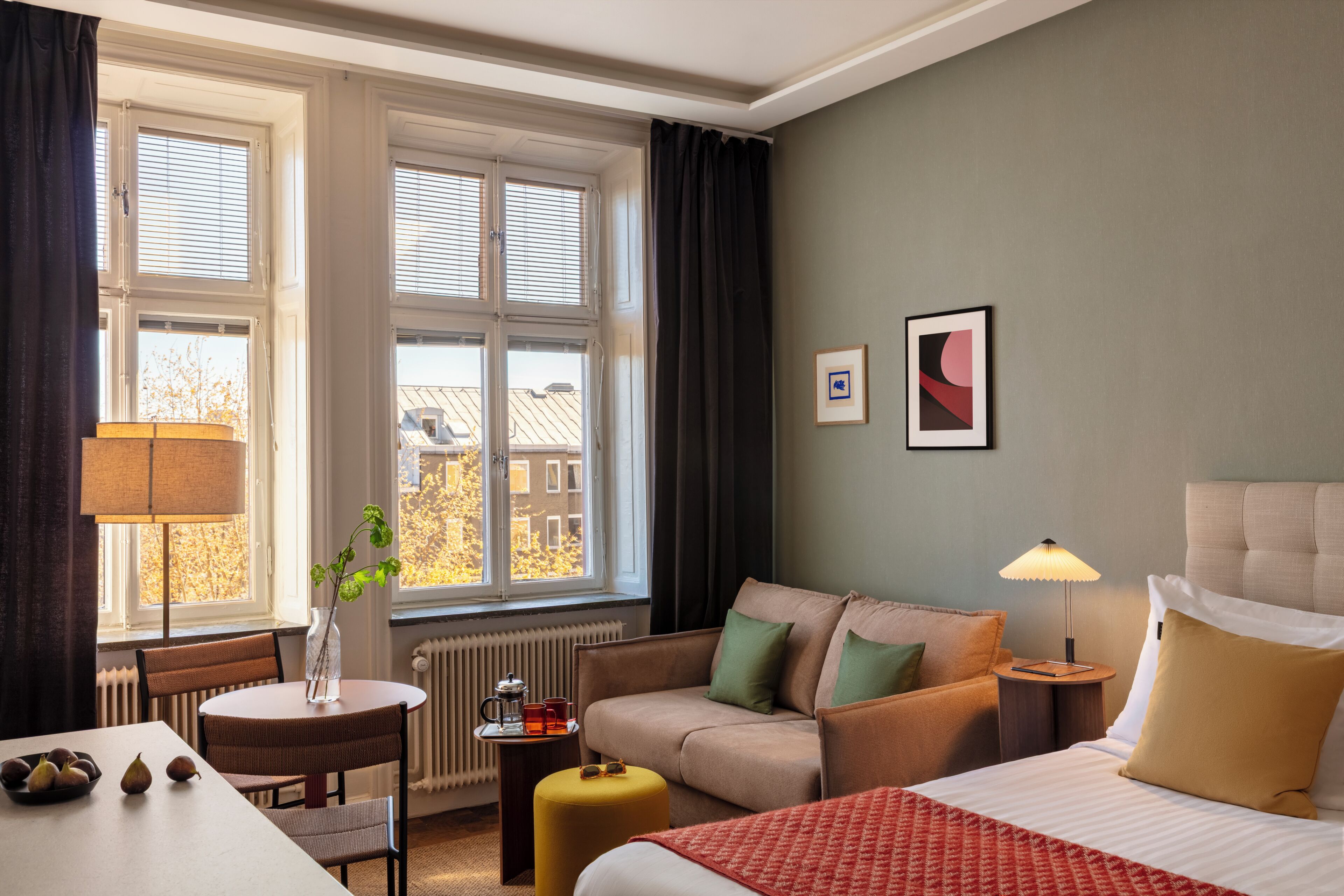 A hotel room with a bed, a sofa, a dining table, and a window with curtains.