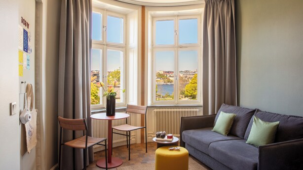 A room with a sofa, chairs, a small table, and a view through large windows. - Bob W Stockholm Sodermalm (Stockholm)