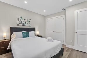 Ein modernes Hotelzimmer mit einem großen Bett, einer Kopfteil, zwei Nachttischen mit Lampen, einem Wandbild und einer Doppeltür.