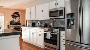 A modern kitchen with white cabinets, stainless steel appliances, and a stone backsplash. - River, Pool, and Jacuzzi in 4 Bedroom House (Three Rivers)