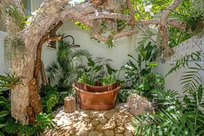 A rustic outdoor area with a large copper bathtub, a tree, and various plants. - Tranquil 4BR Villa Pool Spa Resort Access (Montego Bay)
