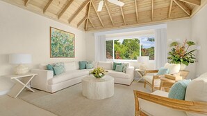 A spacious living room with a high ceiling, white sofas, a round coffee table, and large windows offering a view of greenery. - Tranquil 4BR Villa Pool Spa Resort Access (Montego Bay)